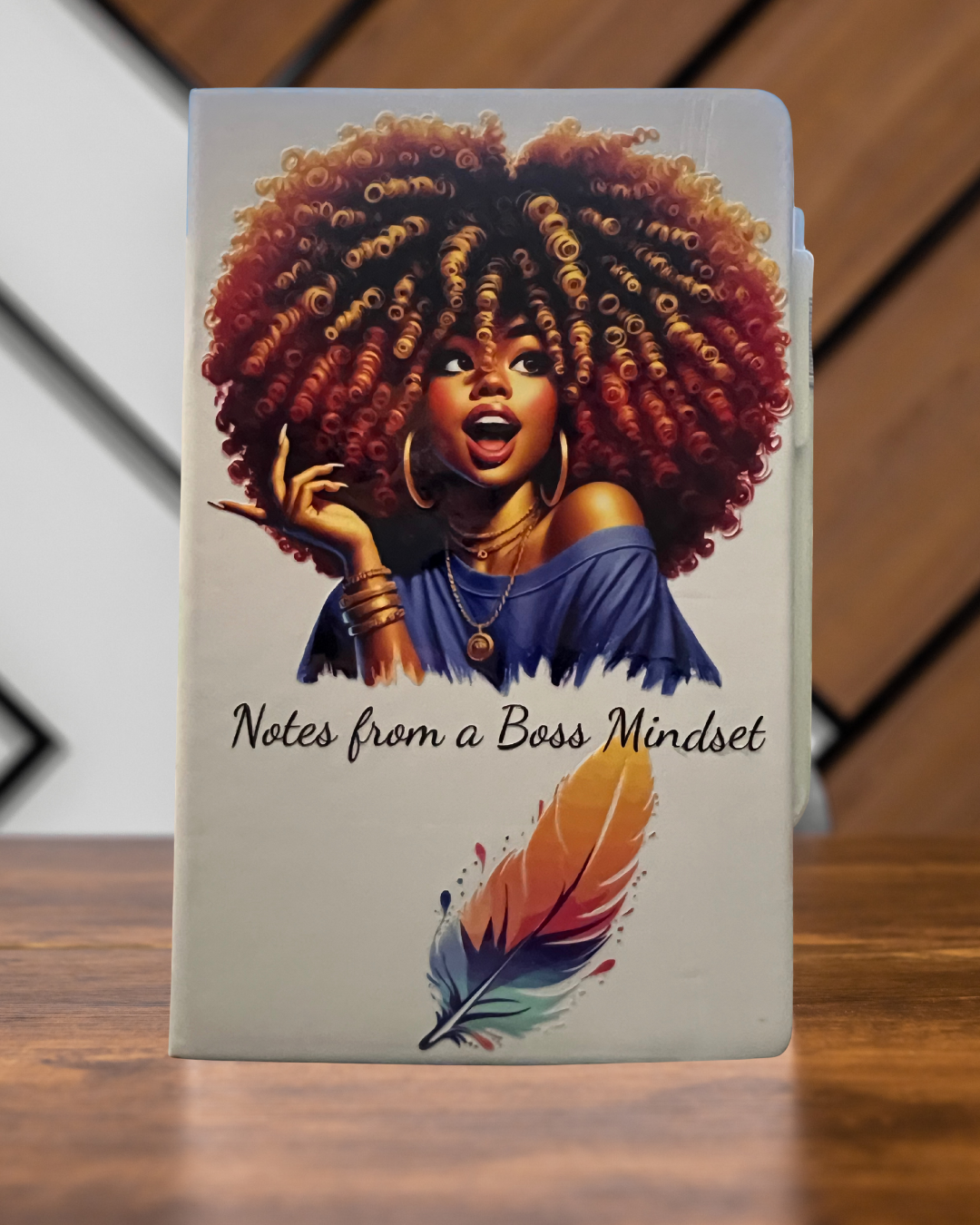 Notebook with a design of a woman with an afro and 'Notes from a Boss Mindset' text on a wooden surface.