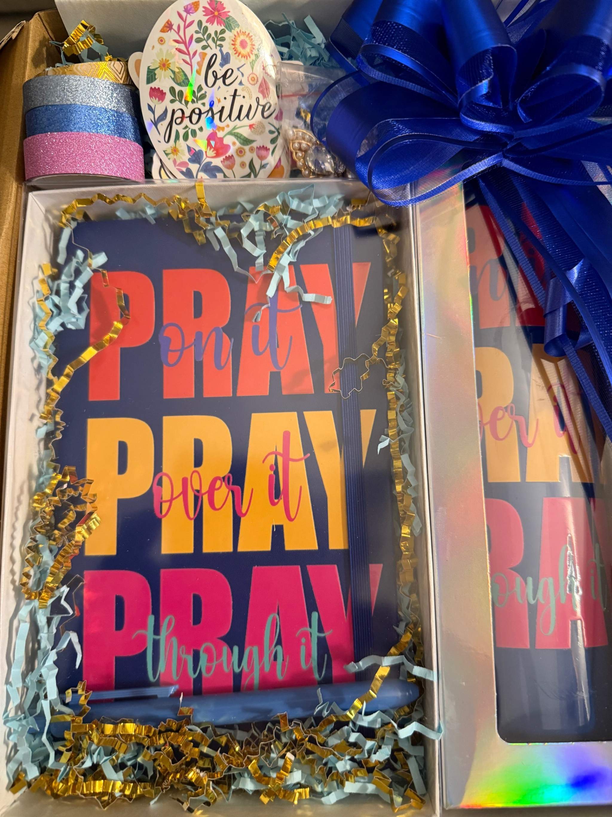 Unboxing gift set featuring a bold “Pray On It, Over It, Through It” journal and matching tumbler in navy, pink, and yellow with decorative ribbon and washi tape.